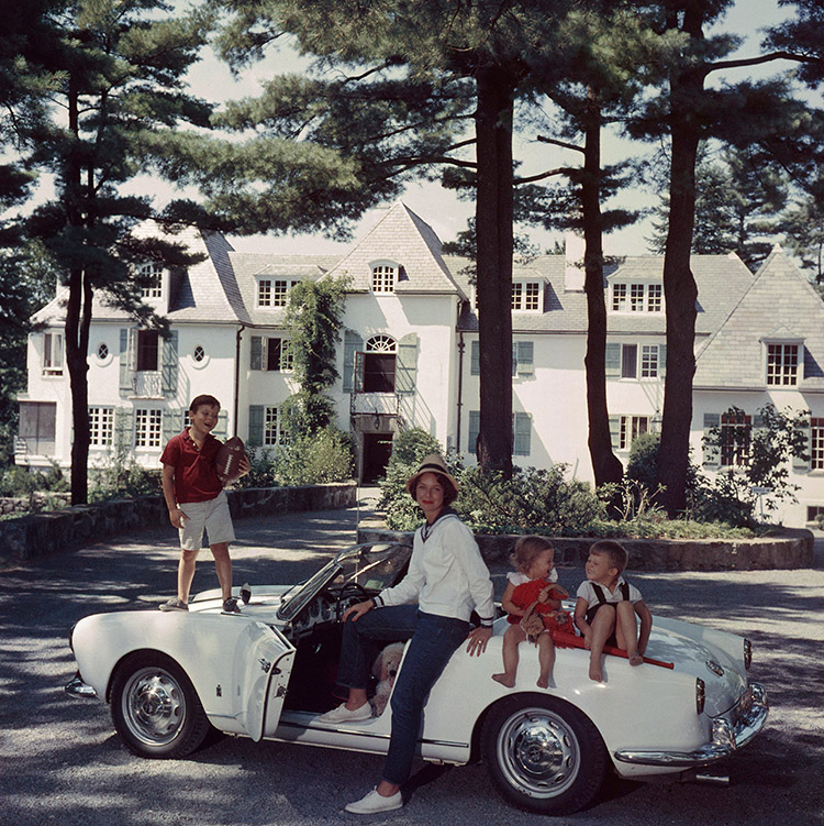 Mrs. Henry Cabot Jr. with her children (left to right) Henry Bromfield Cabot III, Camilla Foote Cabot, and Andrew Hull Cabot, sitting on a car in the driveway of their home, ‘Rollingstones’, Manchester, New Hampshire, circa 1960.